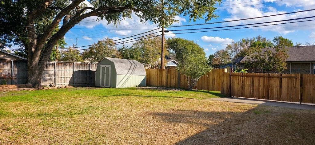 513 Vernet Street, Richardson, TX 75080 Rear yard featuring a grass lawn, perimeter wood fencing, a detached storage shed, and a mature tree