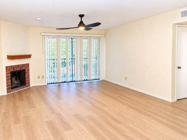 11450 Audelia Road, #104, Dallas, TX 75243 Corner fireplace with red brick surround and wooden mantel, wood-finish flooring, ceiling fan with integrated lighting, and sliding glass doors with vertical blinds