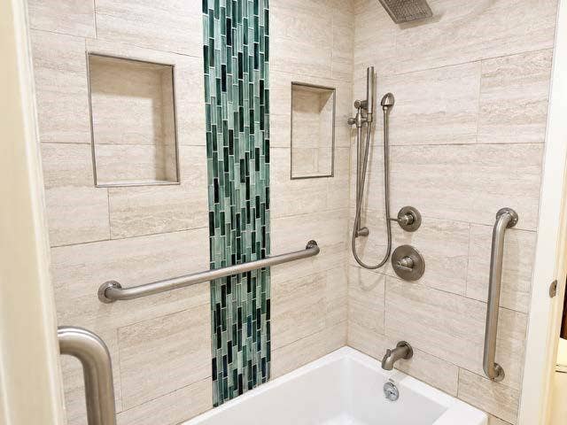 11450 Audelia Road, #104, Dallas, TX 75243 Shower enclosure featuring large-format neutral wall tile, a vertical decorative glass mosaic accent strip, two built-in recessed niches, brushed nickel plumbing fixtures, and integrated support bars
