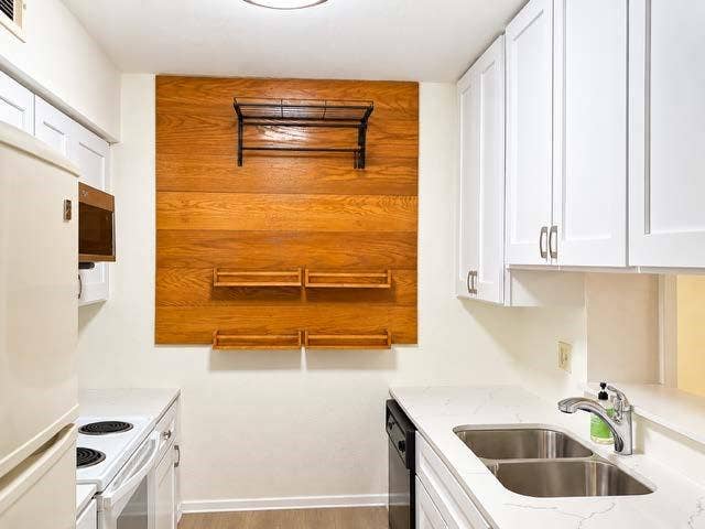 11450 Audelia Road, #104, Dallas, TX 75243 Kitchen featuring white shaker-style cabinetry, quartz countertops, a double-basin stainless steel sink with a chrome faucet, and a decorative wood-finish wall accent with integrated shelving