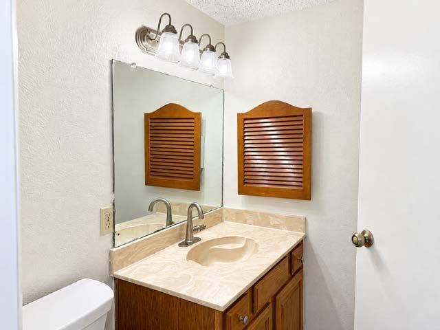 11450 Audelia Road, #104, Dallas, TX 75243 Vanity featuring a light-toned solid surface countertop with an integrated oval sink, wood-finish cabinetry, a wall-mounted louvered storage cabinet, and a four-light brushed-finish vanity fixture