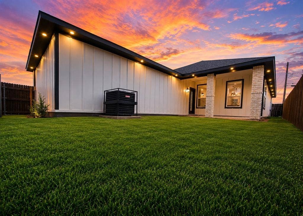 Board-and-batten exterior siding, masonry column accents, recessed soffit lighting, and manicured lawn