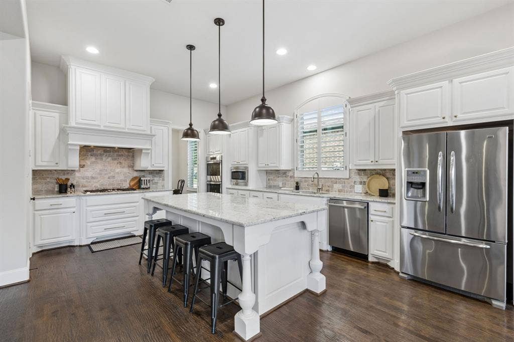 Kitchen featuring white shaker-style cabinetry, stone countertops, brick-style backsplash, stainless steel appliances, and wood-finish flooring