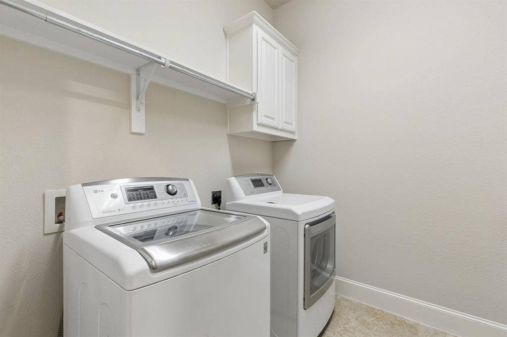 Utility space featuring white shaker-style upper cabinetry, a sturdy wall-mounted shelf with integrated clothing rod, and neutral tile flooring
