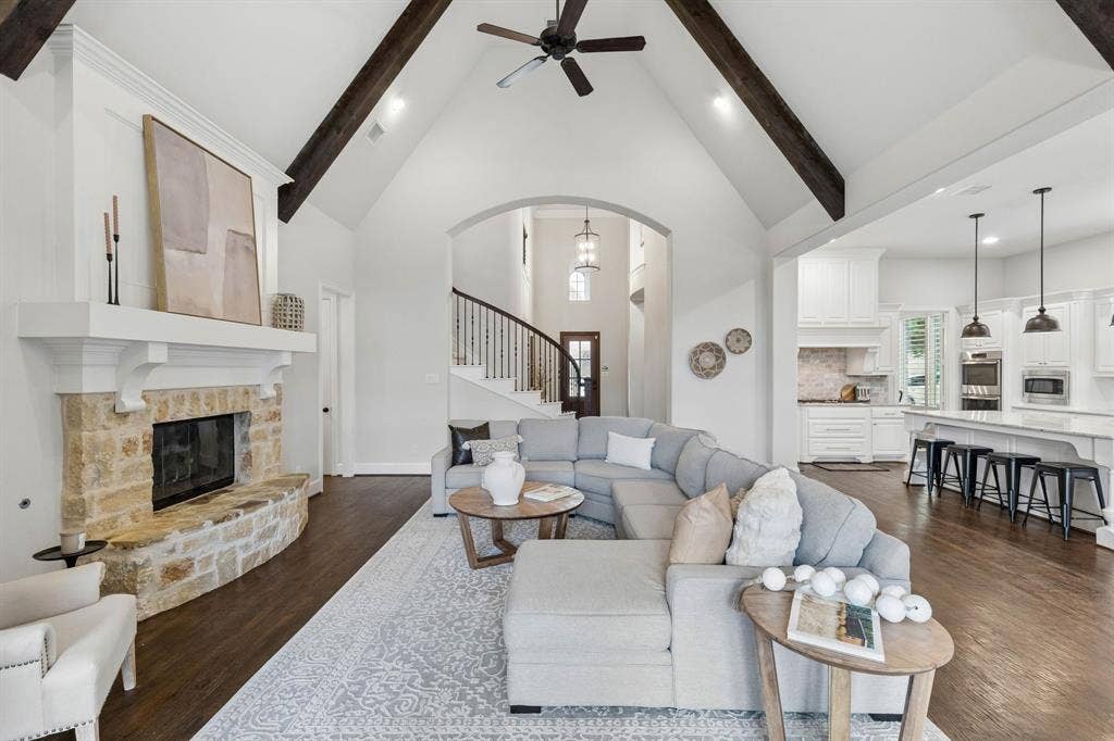 Vaulted ceiling with decorative wood-finish beams, stone-faced fireplace with a mantel, and wood-finish flooring