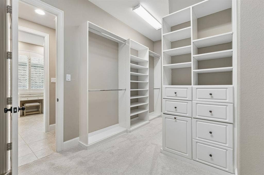 Walk-in closet featuring white built-in shelving, integrated dresser drawers, metal hanging rods, and neutral carpeting