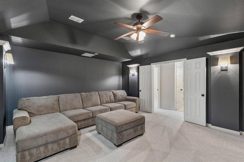Vaulted ceiling featuring a central multi-blade ceiling fan with integrated lighting, wall-mounted light fixtures, and double doors