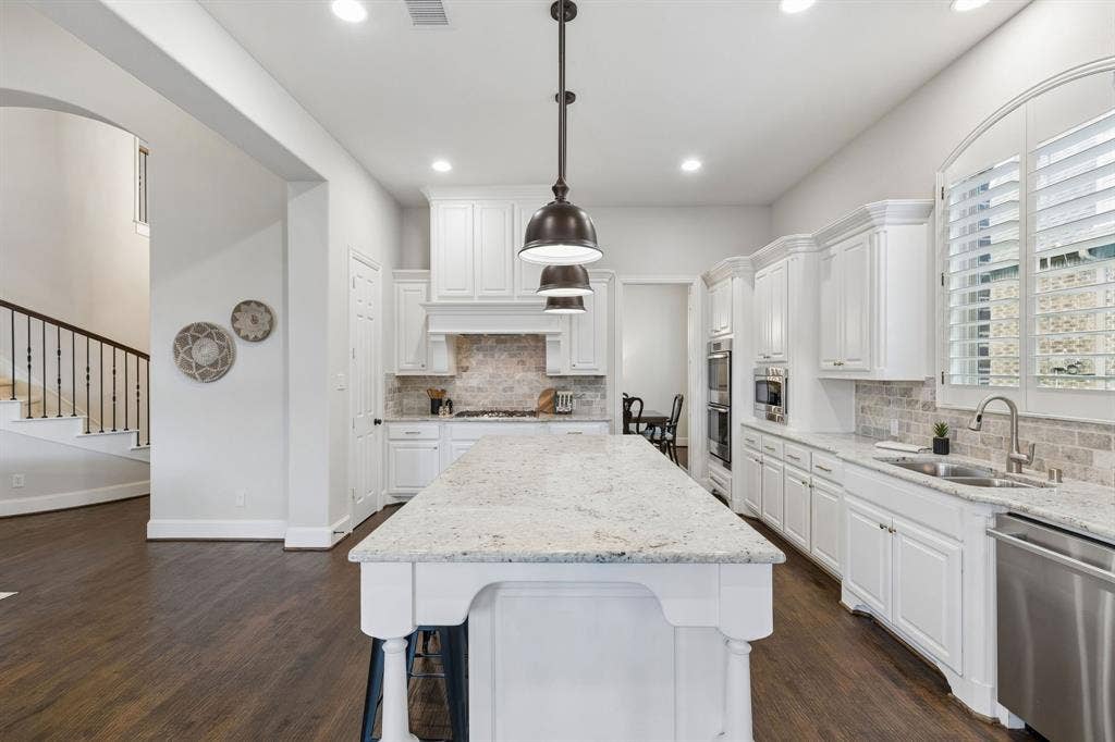 Kitchen featuring a central island with stone countertop, white cabinetry, integrated stainless steel appliances, brick-patterned tile backsplash, and dark wood-finish flooring