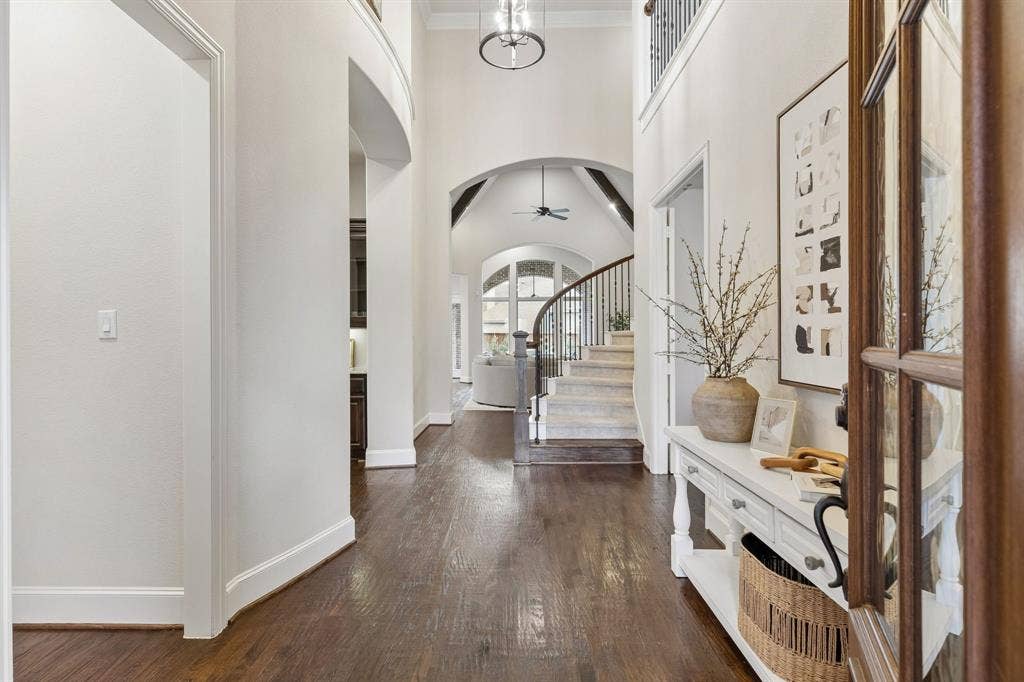 Foyer featuring wood-finish flooring, two-story vaulted ceilings, an arched entryway, and a staircase with wrought iron railings