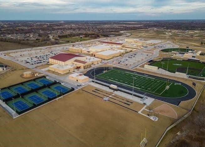 Aerial perspective of athletic facilities featuring multiple fenced tennis courts, a turf football field, track and field infrastructure, and a baseball diamond