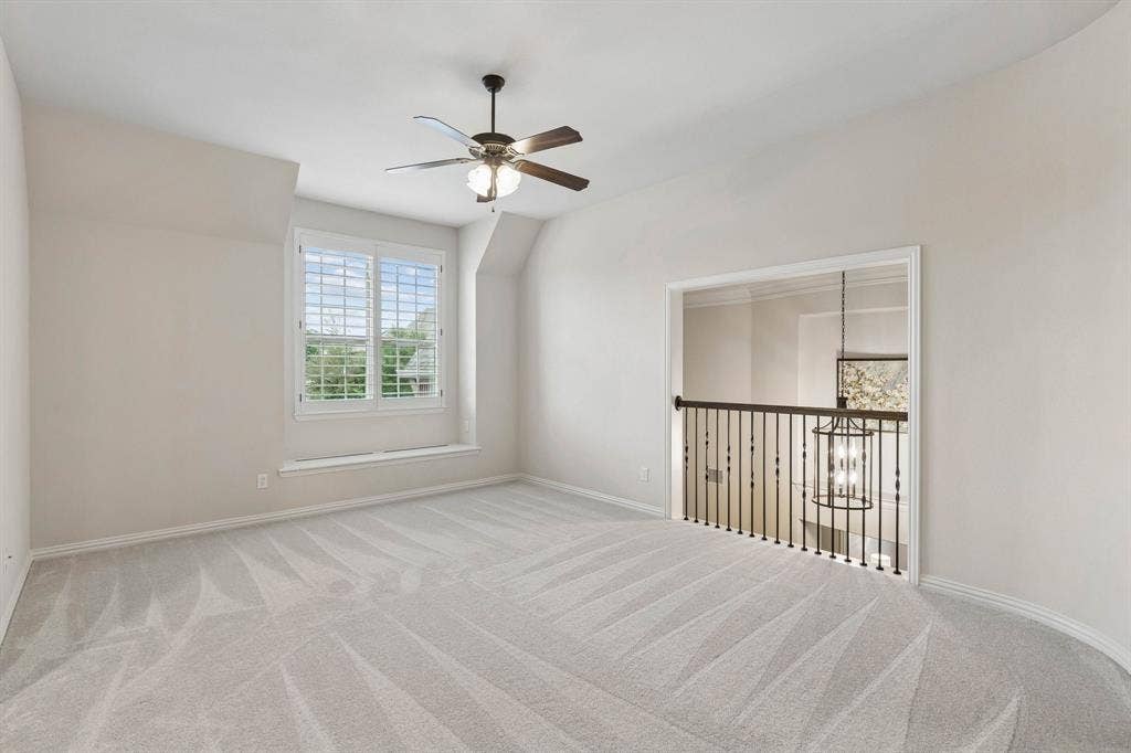 Carpeted room featuring a ceiling fan with integrated lighting, window shutters, a recessed window seat, and iron balusters