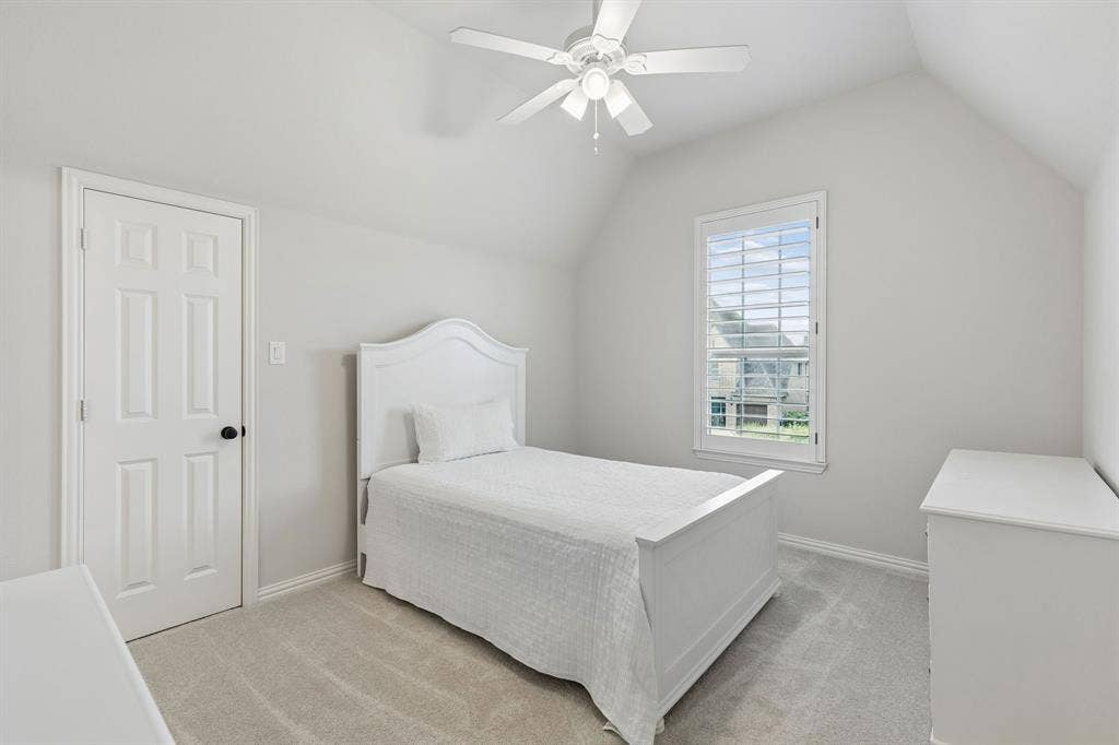 Vaulted ceiling featuring a ceiling fan with integrated lighting, wall-to-wall carpeting, and a window with plantation-style shutters