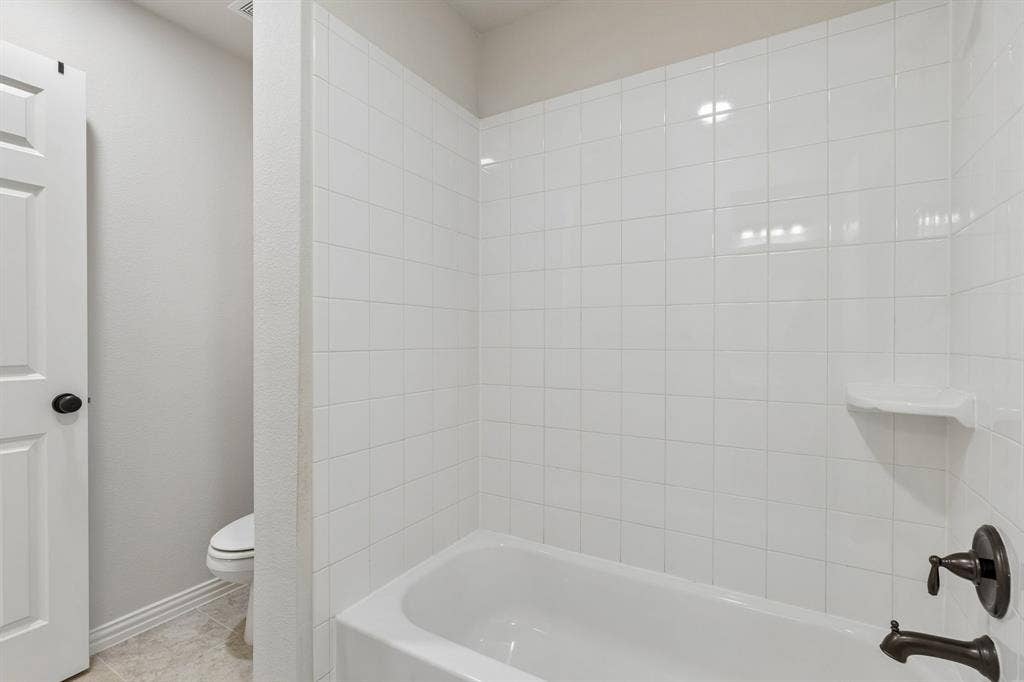 Bathtub enclosure featuring white square tile surround, built-in soap niche, and oil-rubbed bronze faucet hardware