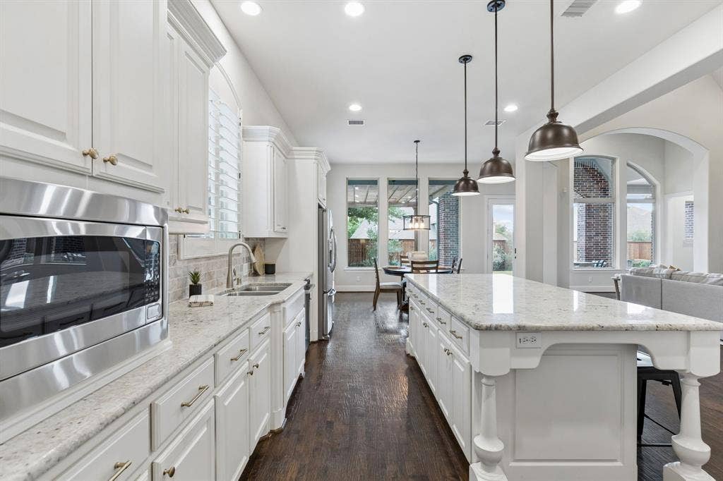 Kitchen featuring white cabinetry, stone countertops, a central island with decorative legs, stainless steel appliances, and wood-finish flooring