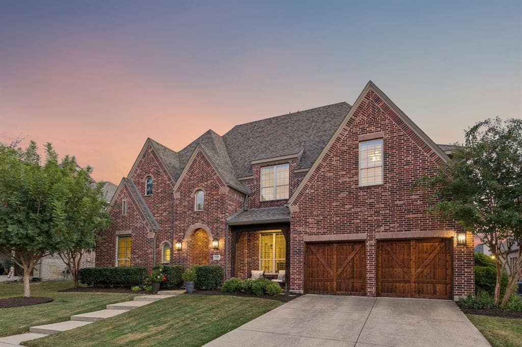 Multi-gable brick exterior featuring an arched entryway, double wood-finish garage doors with carriage-style detailing, and a concrete walkway
