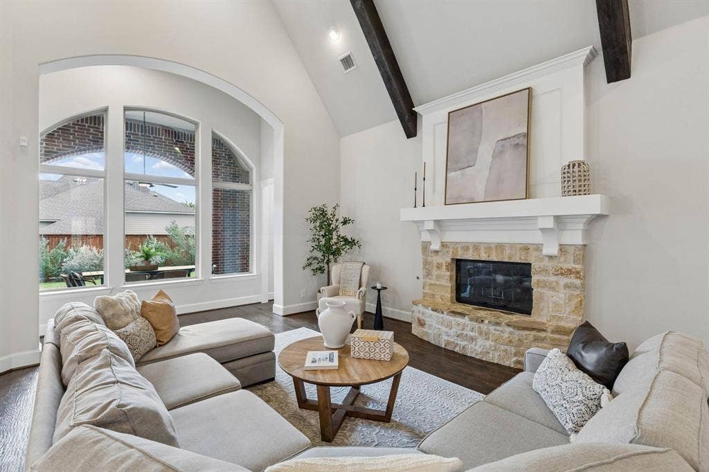 Vaulted ceiling with exposed wood-finish beams, fireplace with natural stone masonry and built-in mantel, and expansive arched window frame