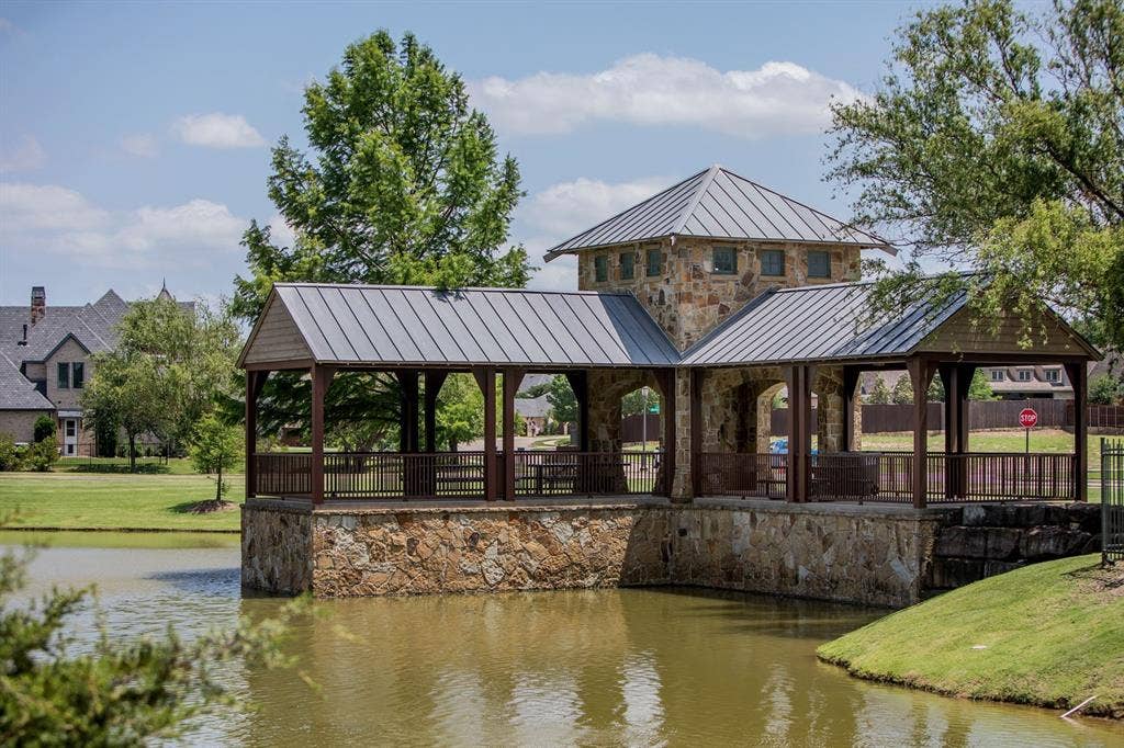 Covered waterfront pavilion featuring natural stone masonry, a metal standing-seam roof, architectural tower, and dark metal railings