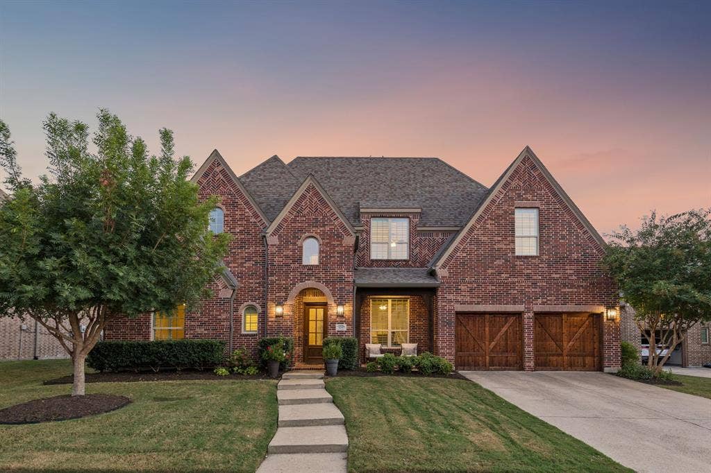 Multi-gabled brick exterior featuring wood-finished carriage-style garage doors, a stone walkway, and shingled roofing