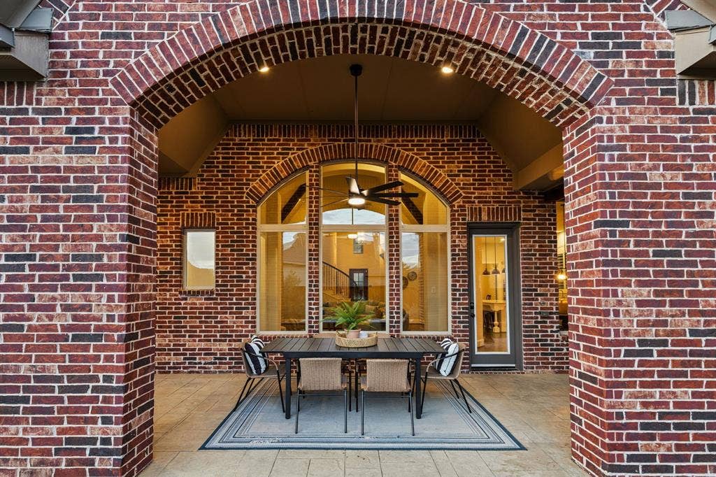 Covered patio featuring red brick masonry, a vaulted ceiling, arched architectural detailing, a central ceiling fan, and large multi-pane windows