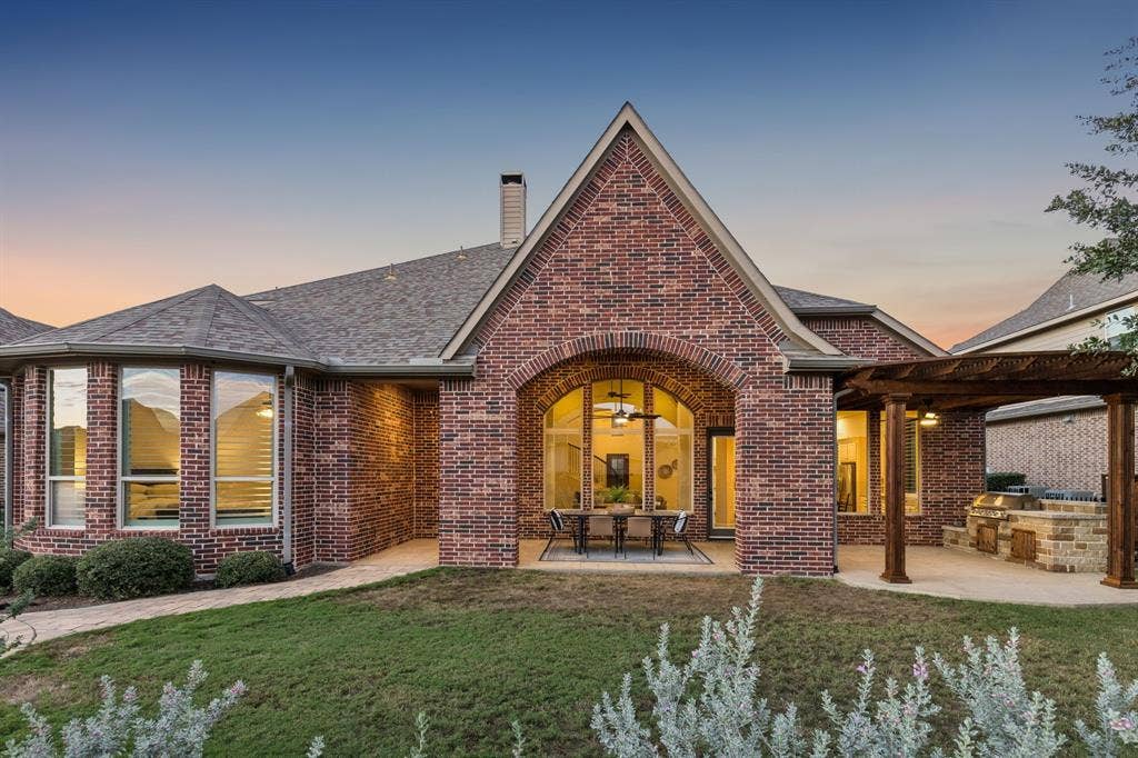 Brick exterior featuring an arched covered patio, attached pergola, built-in masonry grill, and large multi-pane windows