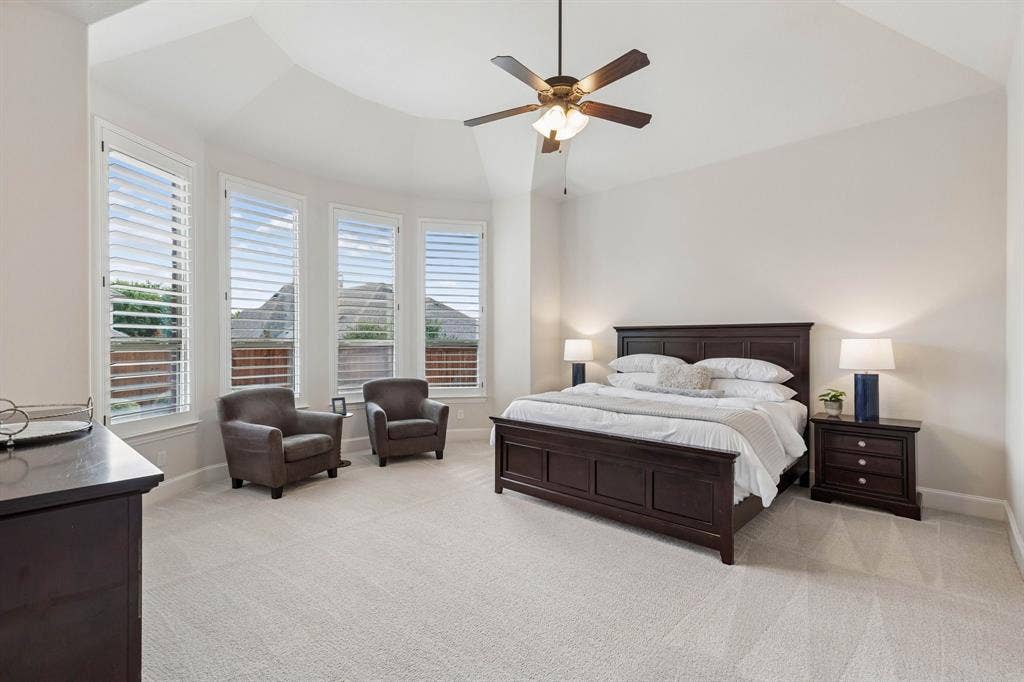 Vaulted ceiling featuring a central lighted ceiling fan, bay window configuration with integrated shutters, and neutral carpeting
