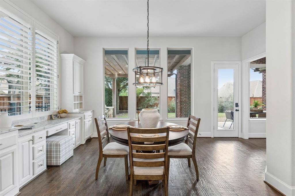 Custom built-in cabinetry featuring light-toned stone surfaces, plantation shutters, dark wood-finish flooring, metal industrial-style pendant lighting, and full-length windows