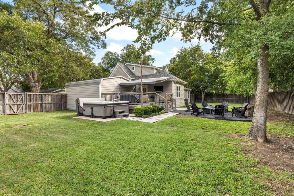 901 Oak Street, McKinney, TX 75069 Spacious backyard featuring a wood-style deck, built-in hot tub, stone-paver walkway, and a designated gravel fire pit area enclosed by wood fencing