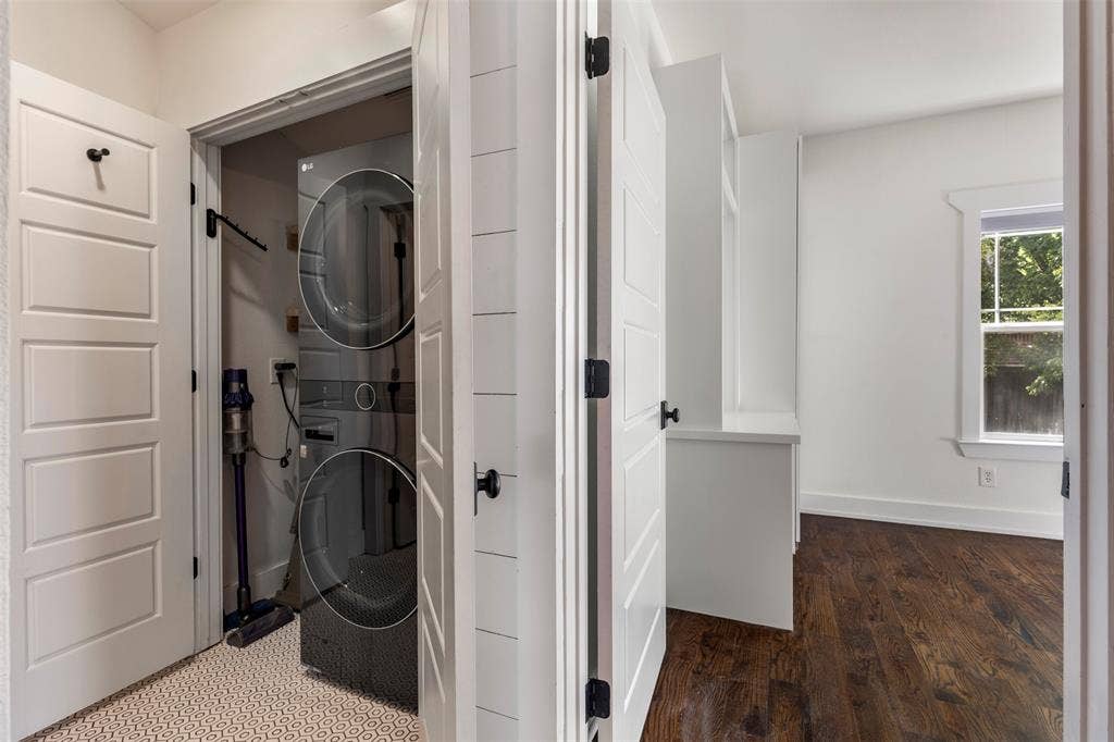 901 Oak Street, McKinney, TX 75069 Built-in laundry closet with stacked appliances, horizontal wall paneling, custom white cabinetry, wood-finish flooring, and a single-hung window with decorative trim