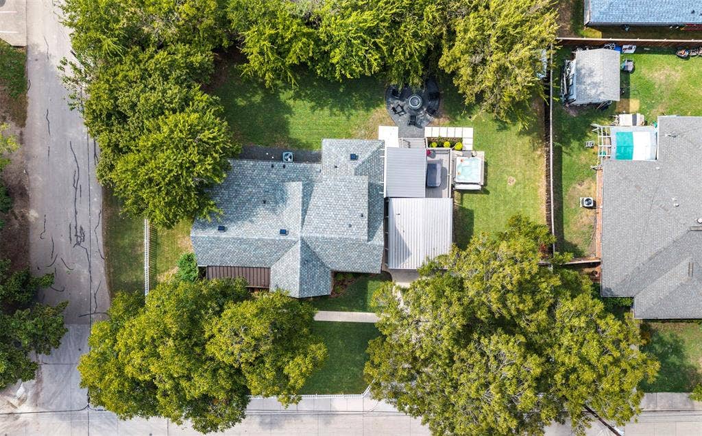 901 Oak Street, McKinney, TX 75069 Aerial perspective featuring a landscaped backyard, a paved circular fire pit area, a built-in spa, a metal-roofed patio cover, and extensive mature tree coverage