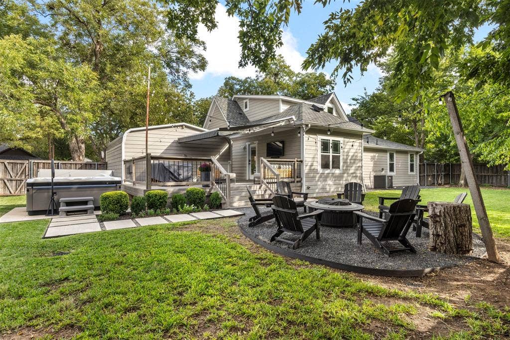 901 Oak Street, McKinney, TX 75069 Expansive backyard featuring a raised wooden deck with metal railing, a built-in hot tub on a concrete pad, a gravel fire pit area, and mature perimeter trees