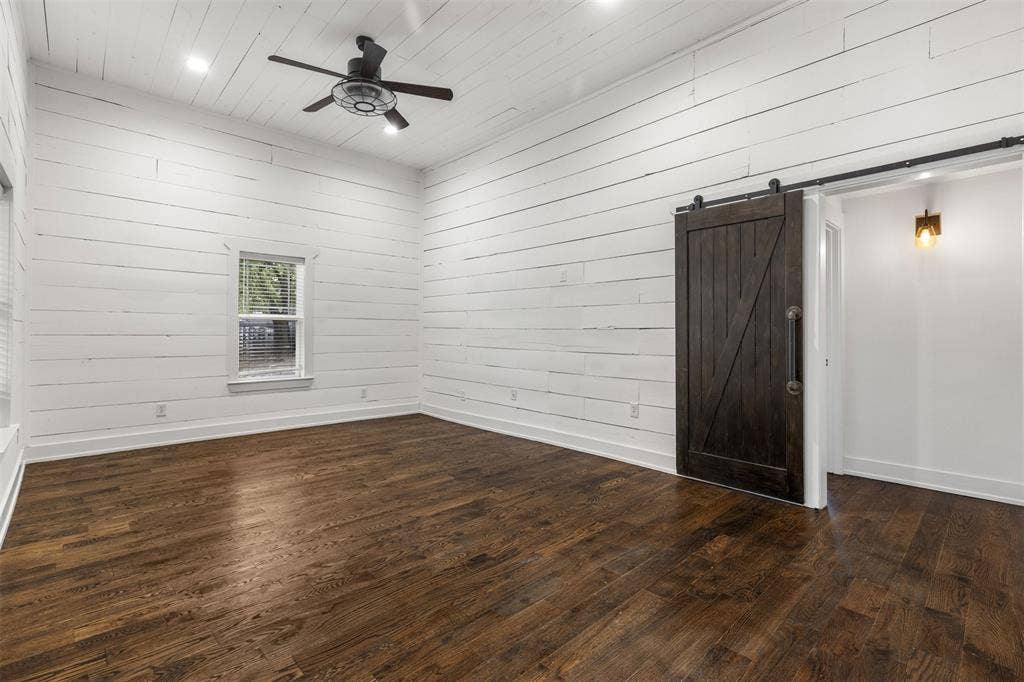 901 Oak Street, McKinney, TX 75069 High ceilings featuring painted horizontal plank wall paneling, dark wood-finish flooring, a dark-stained wood sliding barn door, and a ceiling fan with integrated lighting