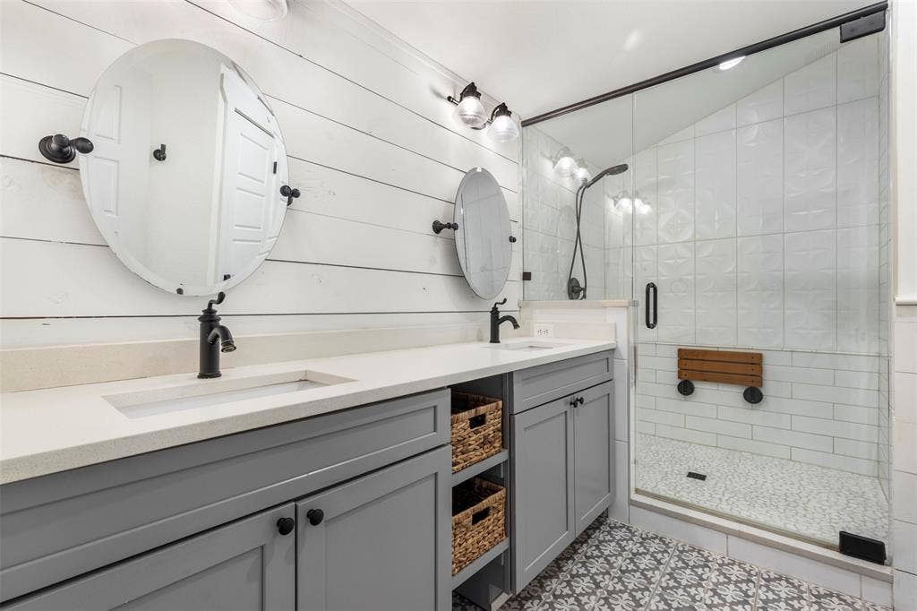 901 Oak Street, McKinney, TX 75069 Double vanity with light-toned solid surface countertops, farmhouse-style shiplap wall paneling, walk-in shower with a glass enclosure, patterned tile flooring, and matte black fixtures