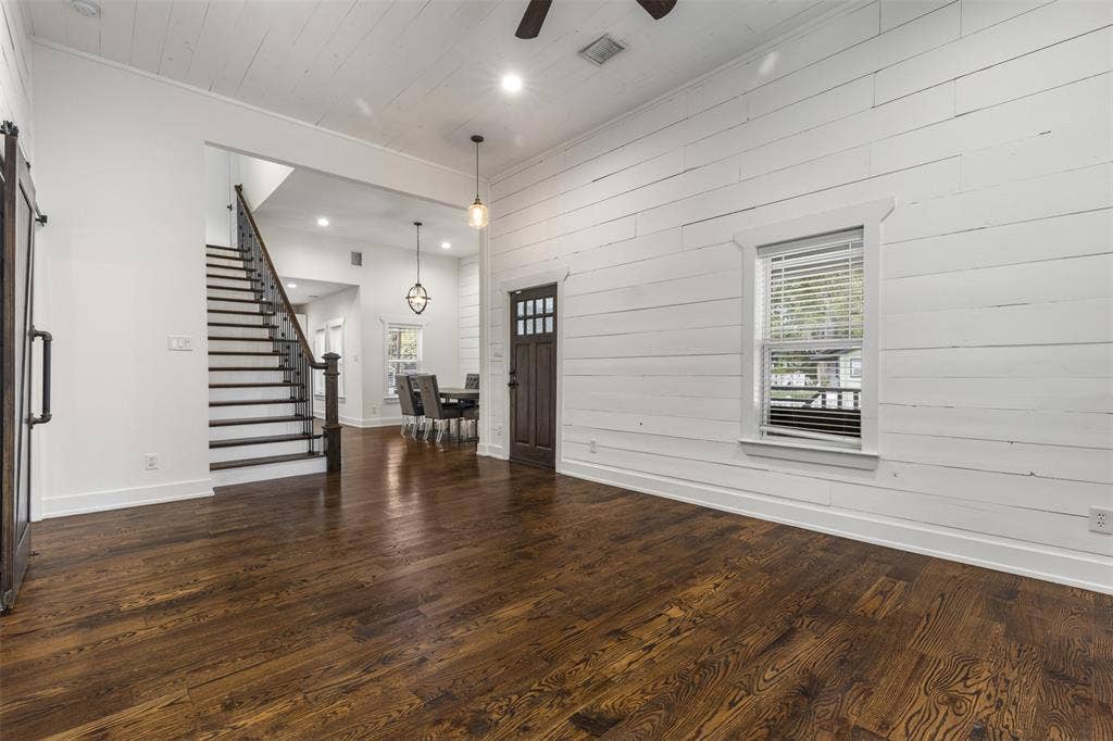 901 Oak Street, McKinney, TX 75069 Interior featuring horizontal wood-plank wall treatments, wood-finish flooring, vaulted ceilings with recessed lighting, and a staircase with stained wood railings