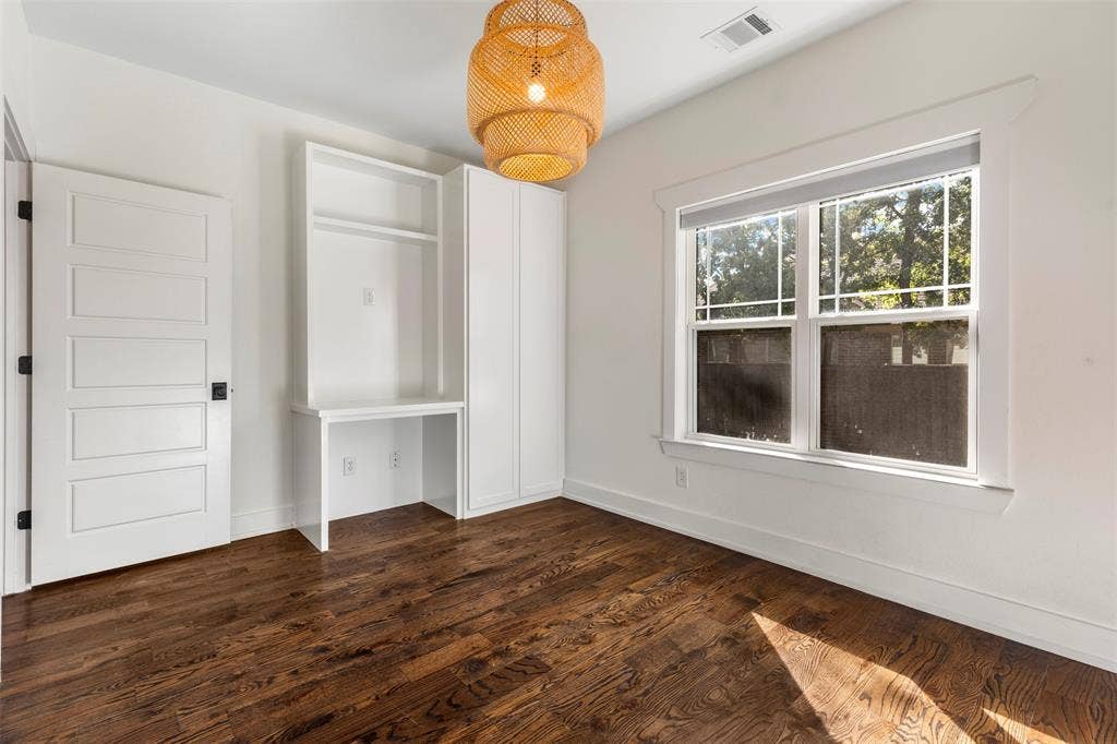 901 Oak Street, McKinney, TX 75069 Room featuring wood-finish flooring, built-in white cabinetry with a desk surface, a multi-pane window with white casing, a five-panel interior door, and a woven pendant light fixture