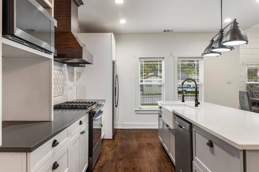 901 Oak Street, McKinney, TX 75069 Kitchen featuring a large island with a farmhouse sink, stone countertops, custom cabinetry, wood-finish flooring, and a decorative tile backsplash
