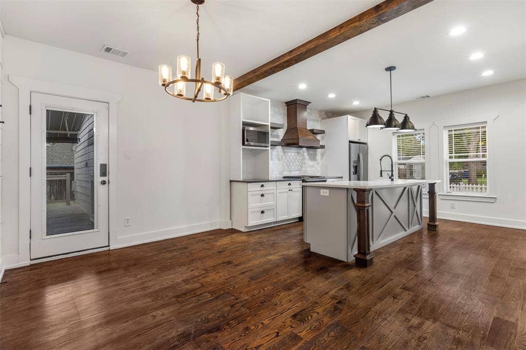 901 Oak Street, McKinney, TX 75069 Kitchen featuring wood-finish flooring, a central island with X-brace detailing, custom cabinetry, a wood-trimmed range hood, and overhead pendant lighting
