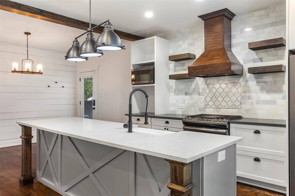 901 Oak Street, McKinney, TX 75069 Kitchen featuring a center island with quartz countertop, custom wood-finish range hood, decorative tile backsplash, open wood shelving, and multi-light industrial-style pendant fixtures
