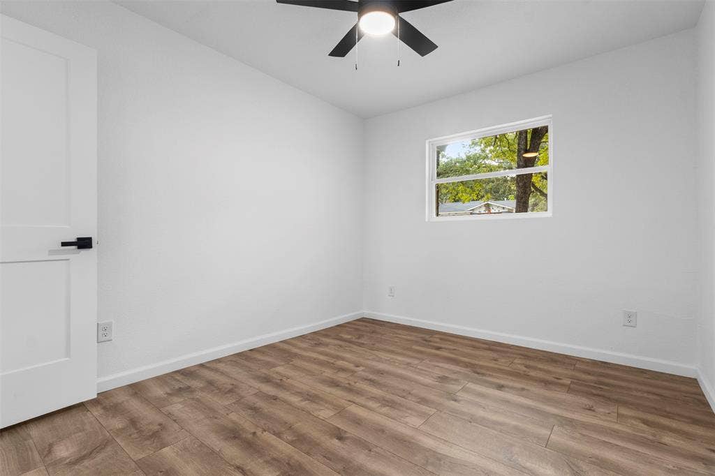 4813 Alandale Drive, Forest Hill, TX 76119 Room featuring wood-finish flooring, a matte black ceiling fan with an integrated light fixture, a single-panel interior door with matte black hardware, and a single-pane window