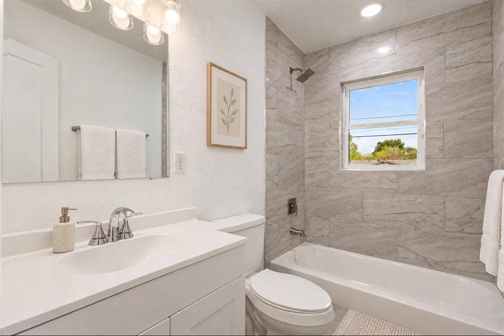 4813 Alandale Drive, Forest Hill, TX 76119 Bathroom featuring a white vanity with a rectangular basin, large wall-mounted mirror, recessed lighting, and a shower-tub combination with horizontal stone-finish tile surround and metallic hardware
