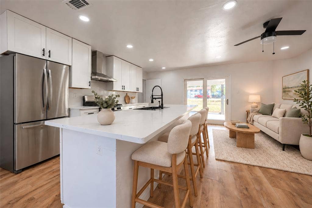 Kitchen featuring white cabinetry, an expansive center island with a stone-finish countertop, stainless steel refrigerator, stainless steel range hood, and wood-finish flooring