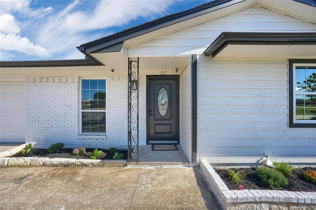Exterior facade featuring painted white brick masonry, horizontal siding, decorative wrought iron porch column, and a dark-toned front entry door with oval glass inlay