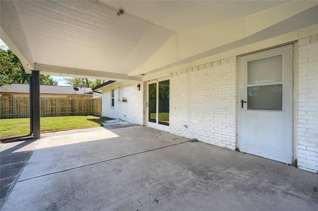 Covered concrete patio featuring painted brick exterior, glass-paneled entry door, and sliding glass door