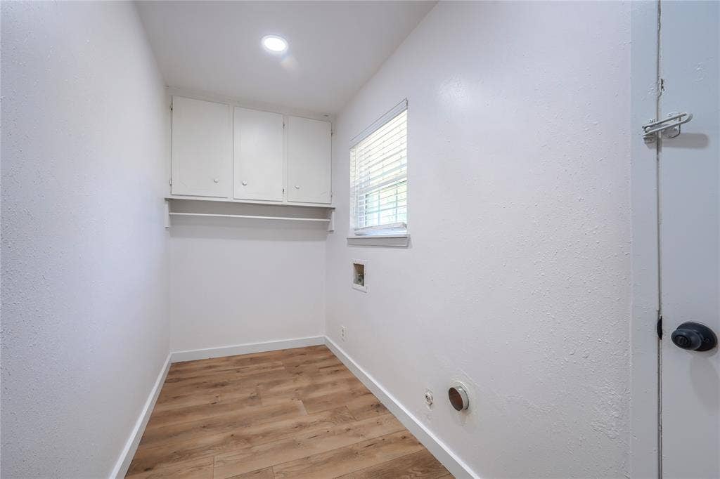 Utility space featuring wood-finish flooring, white upper wall-mounted cabinetry, a recessed lighting fixture, and a window with horizontal blinds