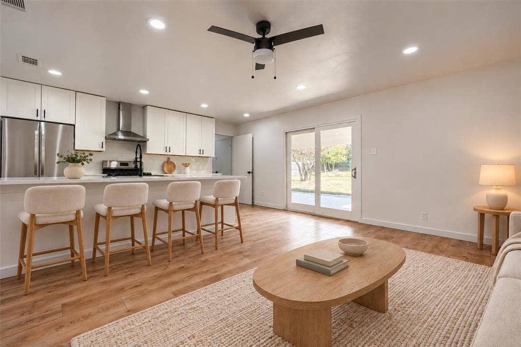 Kitchen featuring white shaker cabinetry, stainless steel appliances, a center island with a breakfast bar, recessed lighting, and wood-finish flooring throughout the open-concept space