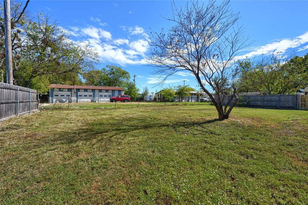 Expansive open lot featuring a perimeter wood fence, grass terrain, and mature trees