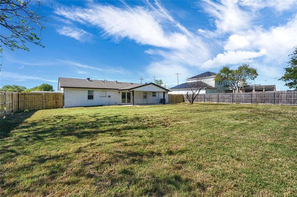 Expansive backyard featuring a large grass lawn, perimeter wood privacy fencing, and a covered patio