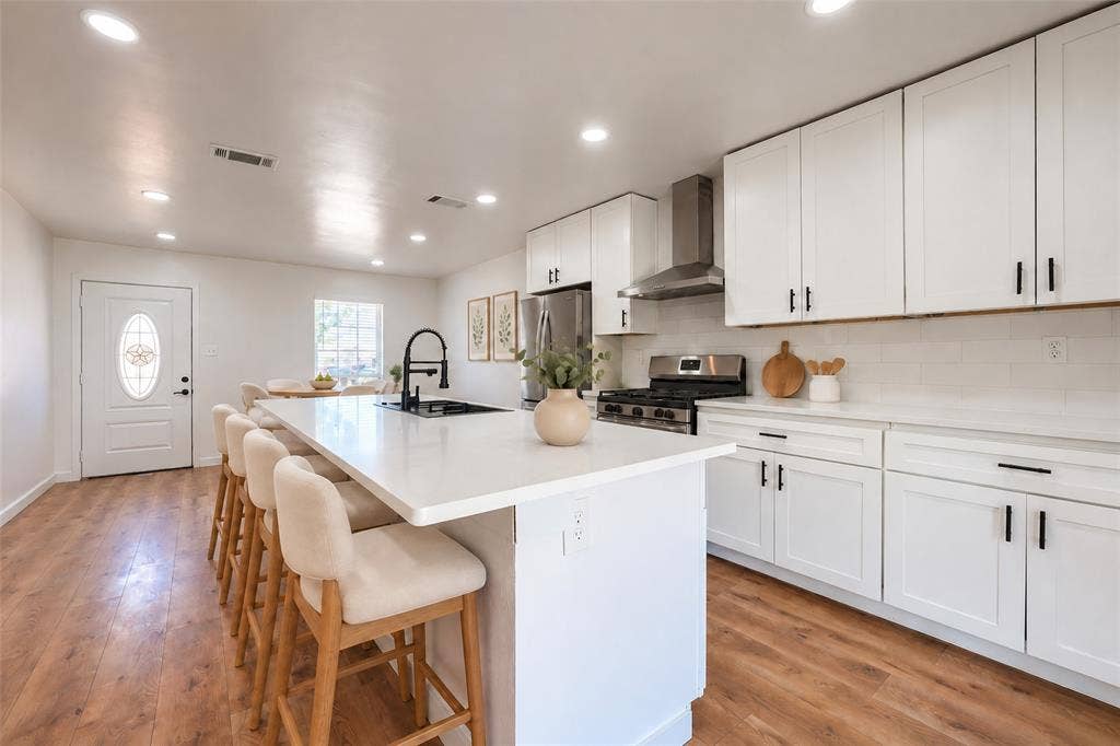 Kitchen featuring white shaker-style cabinetry, quartz countertops, a central island with a matte black faucet, stainless steel appliances, and wood-finish flooring