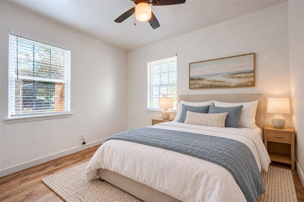 Wood-finish flooring, dual windows with horizontal blinds, and a ceiling-mounted light fixture with a fan