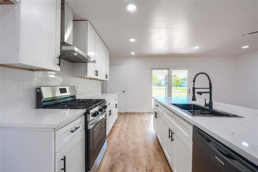 Kitchen featuring white cabinetry, quartz countertops, white subway tile backsplash, stainless steel gas range, and a center island with a matte black faucet