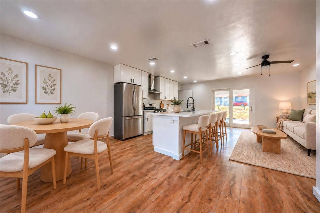 Open-concept area featuring wood-finish flooring, white cabinetry, a center kitchen island with bar seating, stainless steel appliances, and recessed lighting